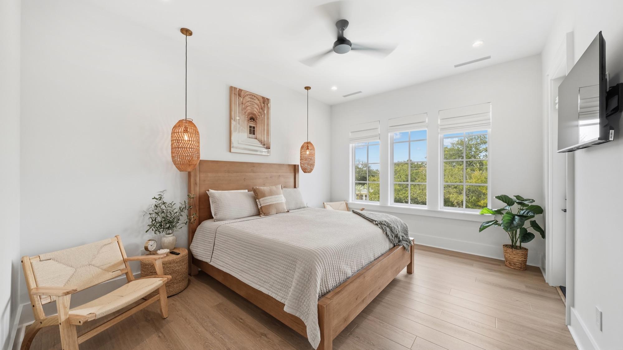 Bright primary bedroom with a wood bed, rattan pendants and plants, photographed on the Florida Panhandle