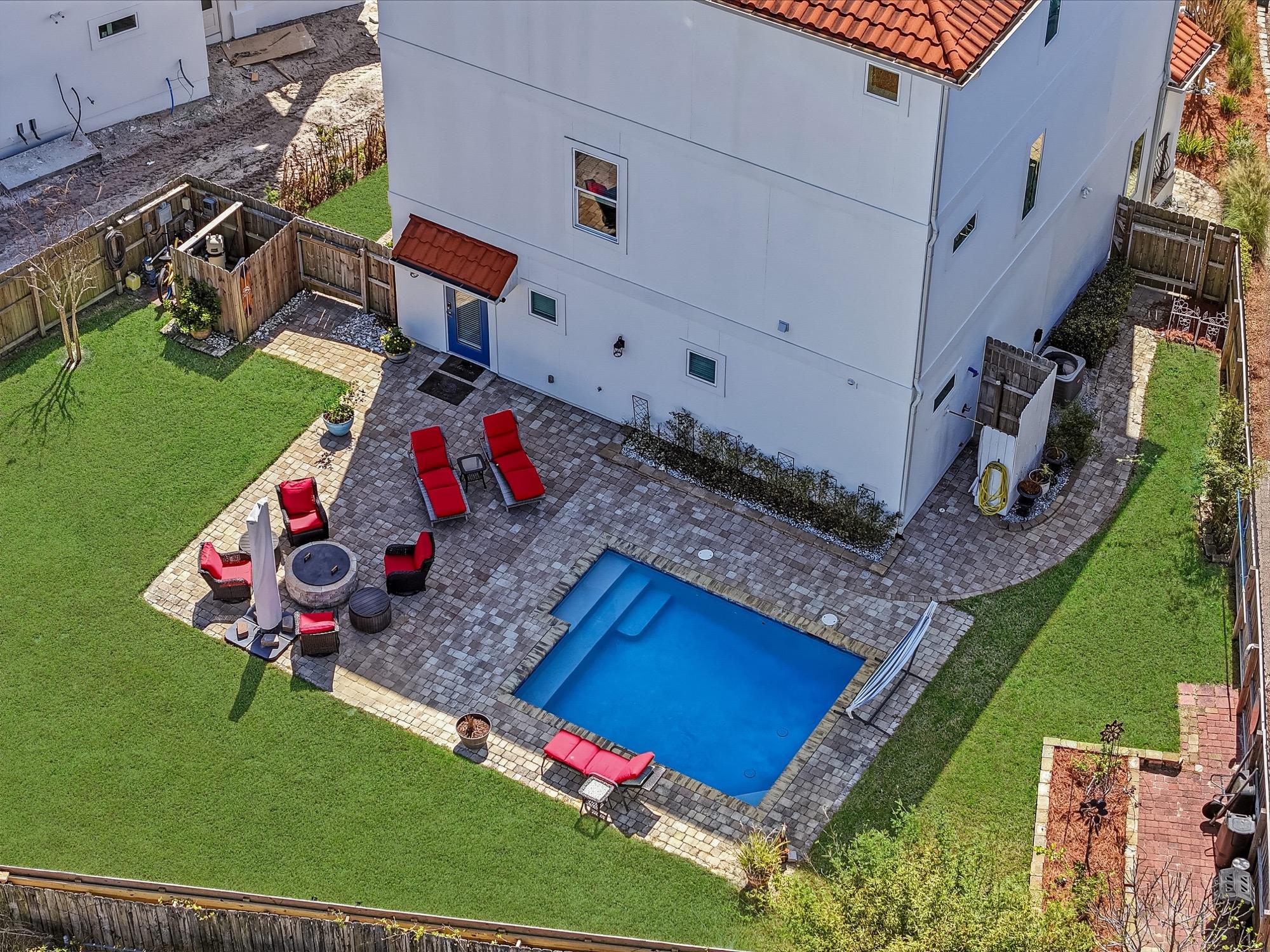 Aerial view of a backyard pool, turf lawn and red lounge chairs, photographed on the Florida Panhandle