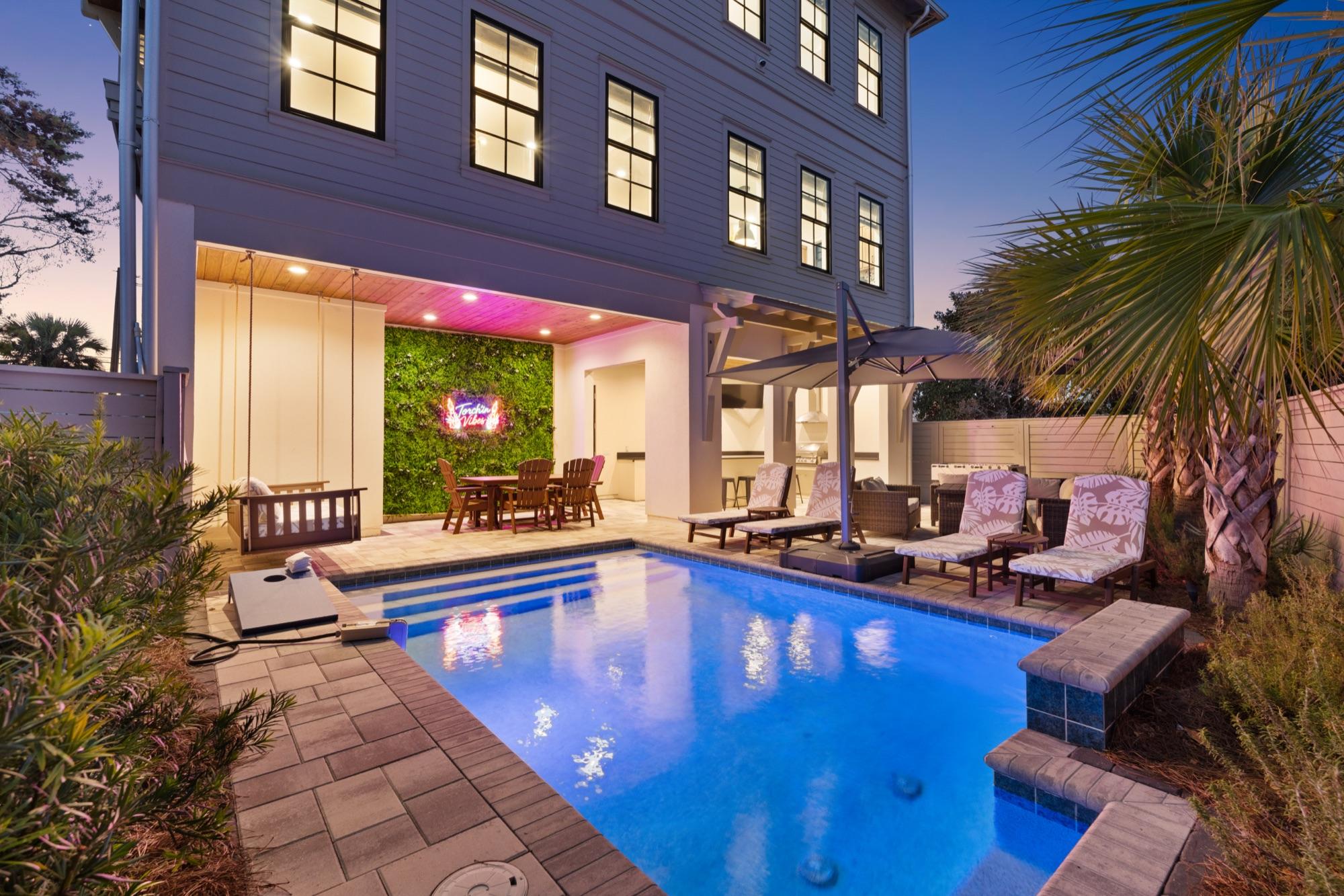 Backyard pool lit up at twilight beside a white coastal home, photographed on the Florida Panhandle