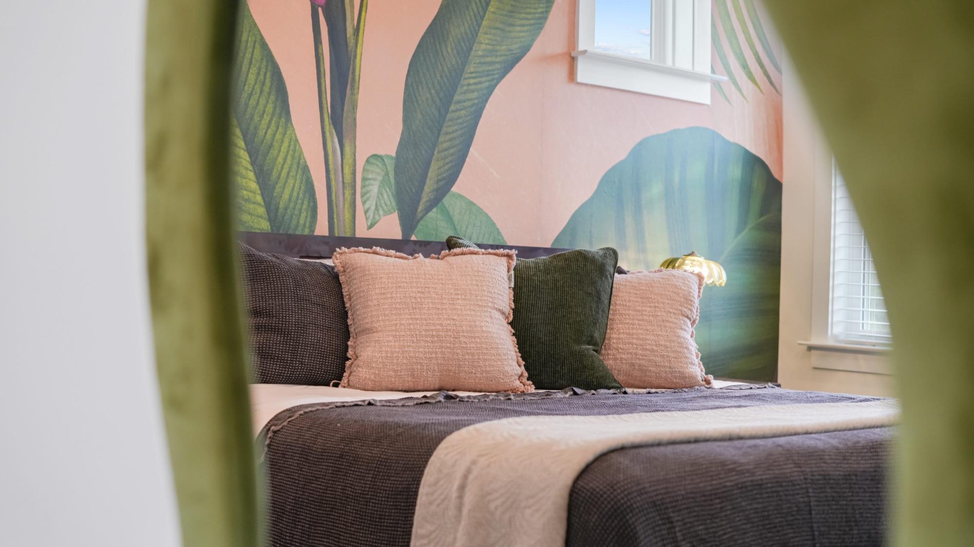 Velvet throw pillows on a bed against a pink tropical mural, photographed on the Florida Panhandle
