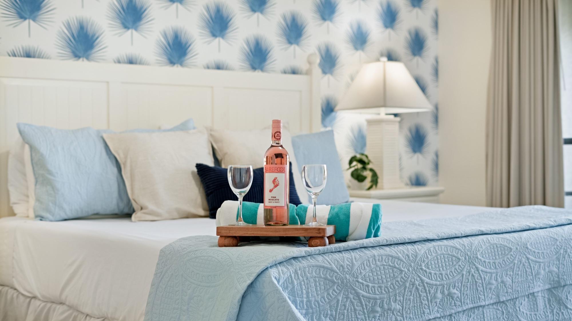 Bed styled with a breakfast tray and wine glasses against blue botanical wallpaper, photographed on the Florida Panhandle