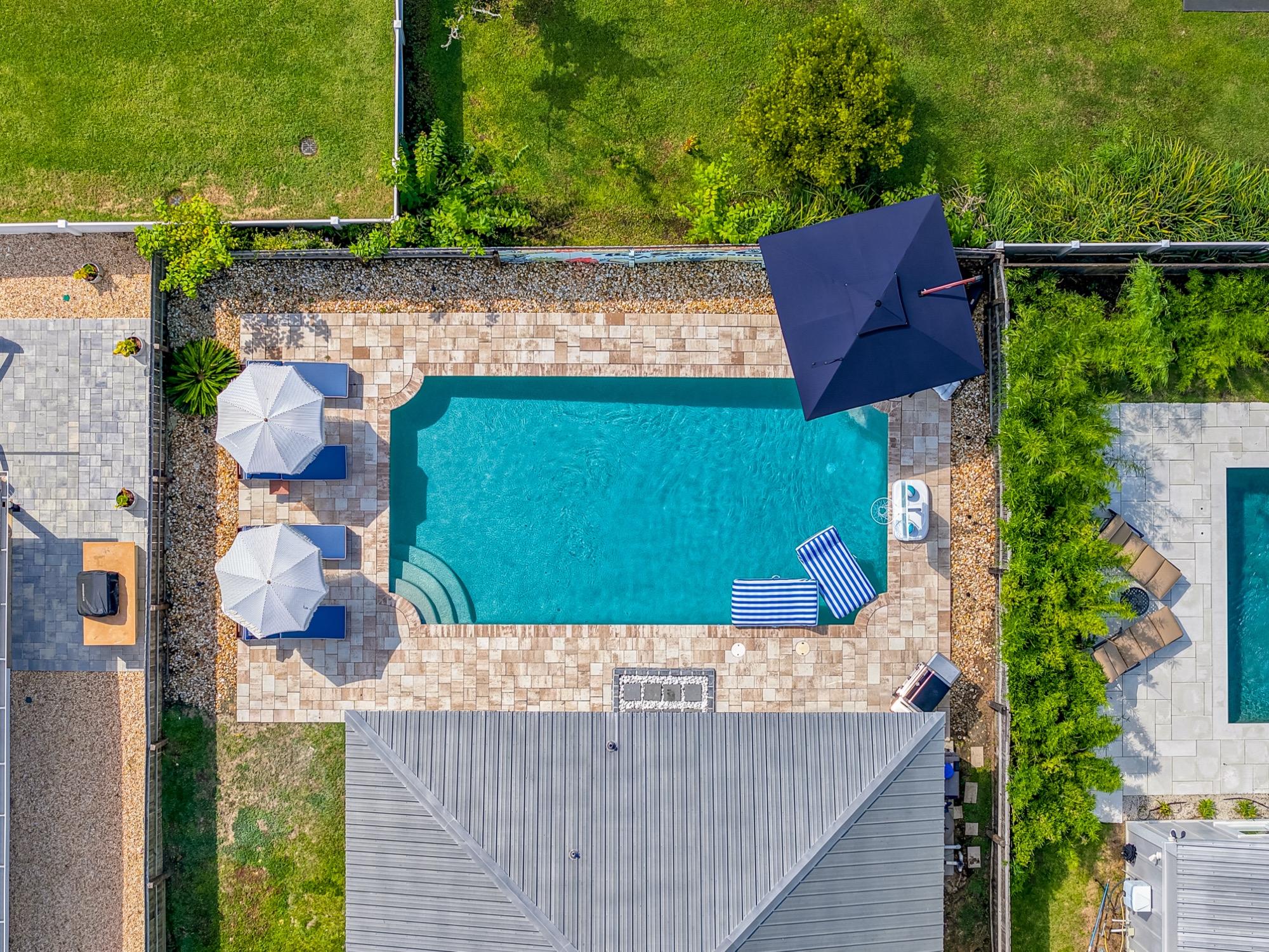 Top-down aerial of a backyard pool with cabanas and umbrellas, photographed on the Florida Panhandle