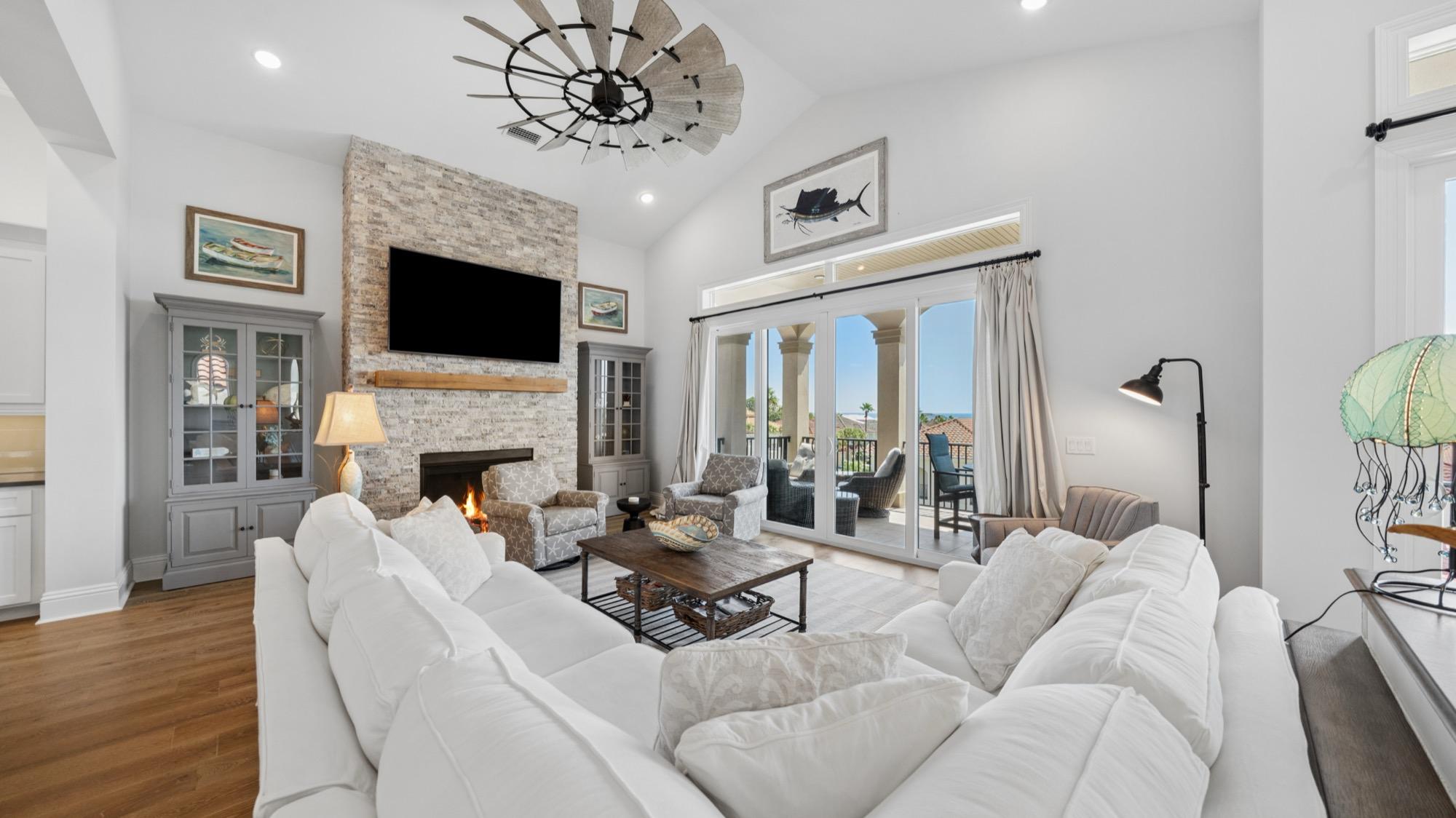 Living room with a white sectional, stone fireplace and a windmill ceiling fan, photographed on the Florida Panhandle