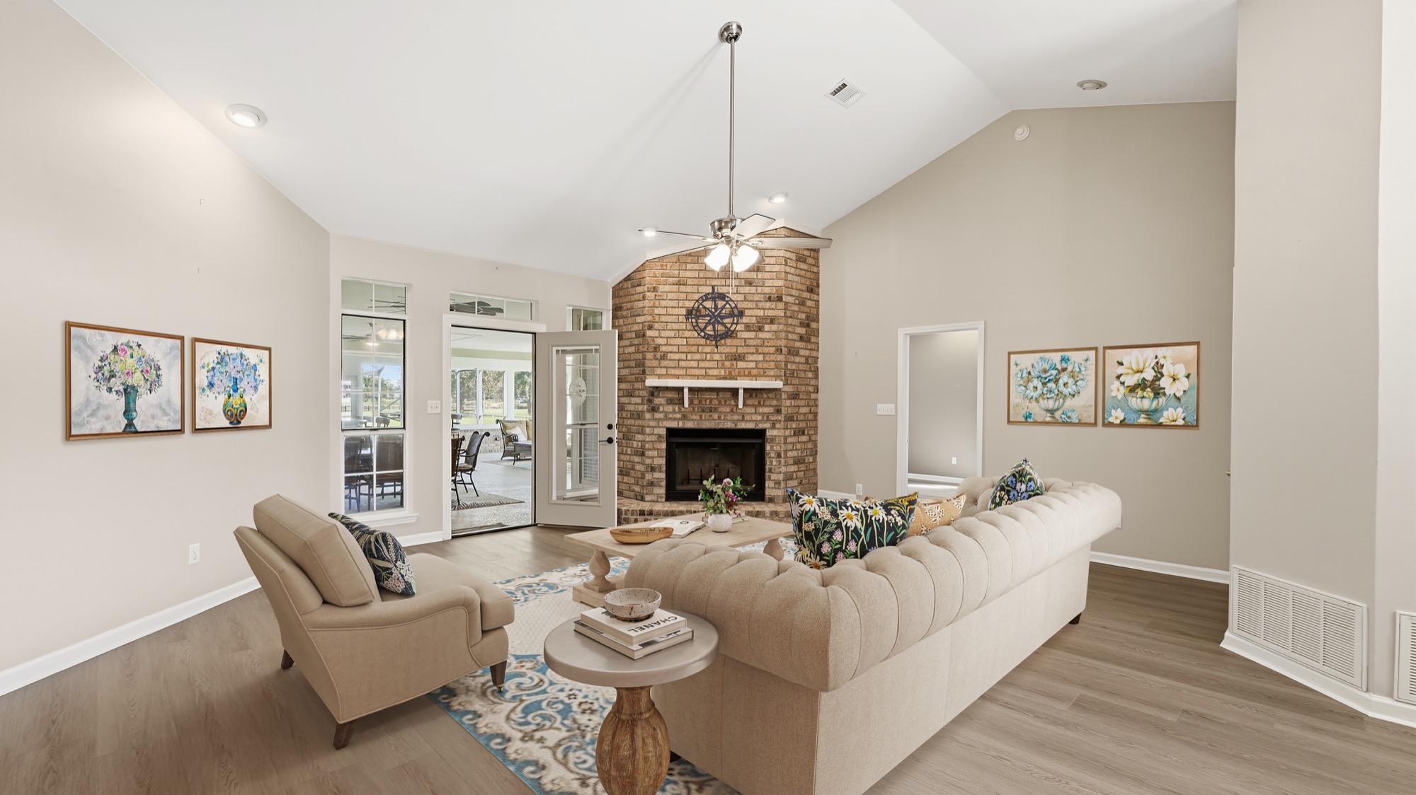 Virtually staged living room with a tufted sofa and brick corner fireplace, photographed on the Florida Panhandle