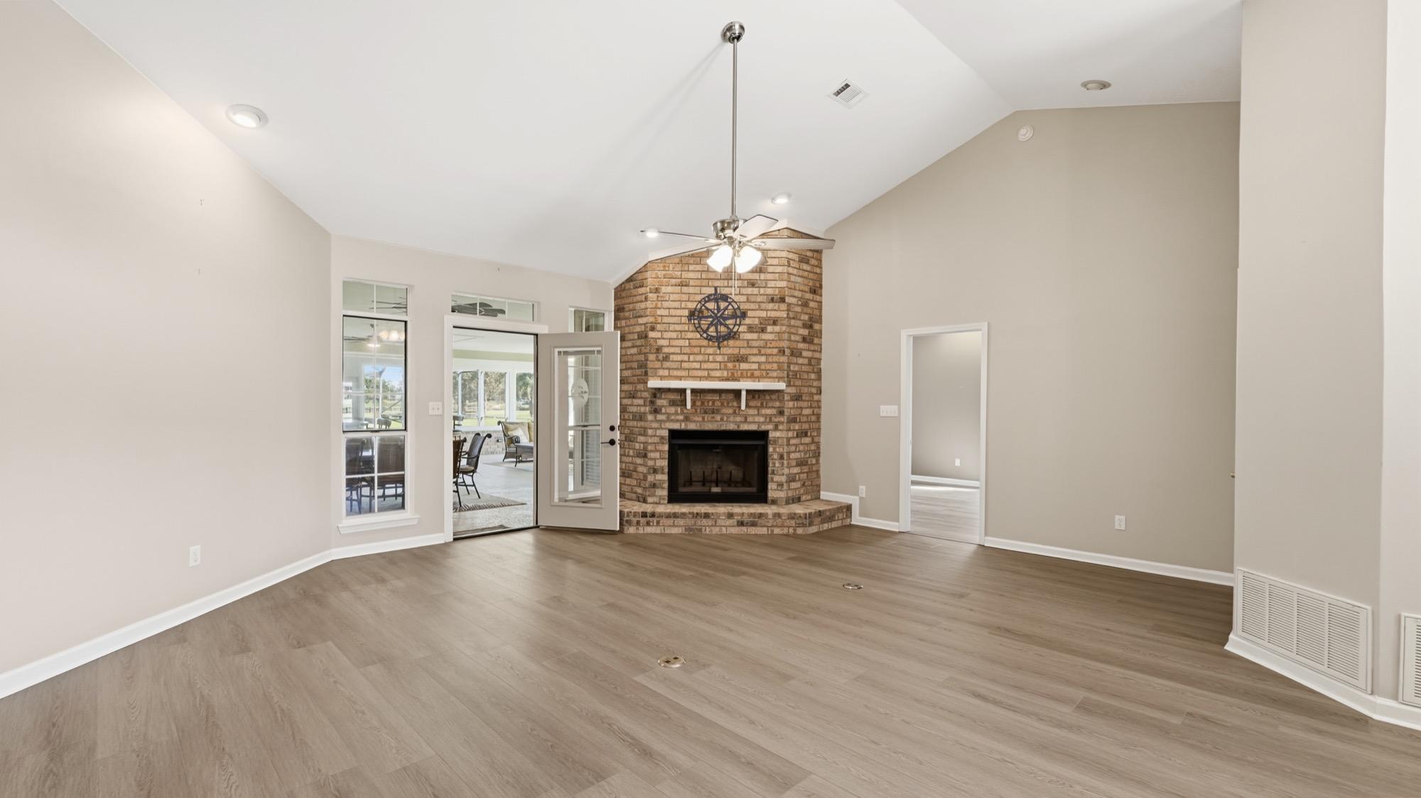 Empty living room with a brick corner fireplace and vaulted ceiling, before staging, photographed on the Florida Panhandle